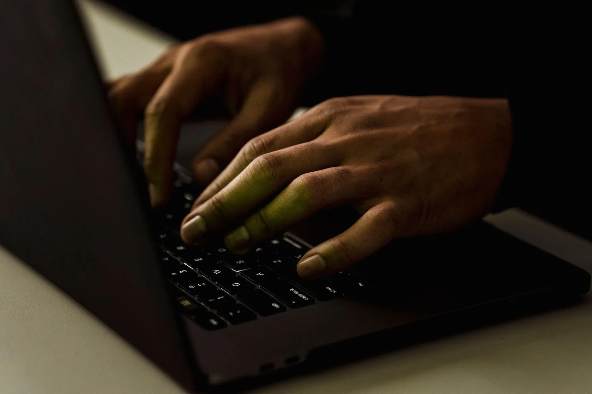 Close-up of hands typing on a laptop keyboard in low light