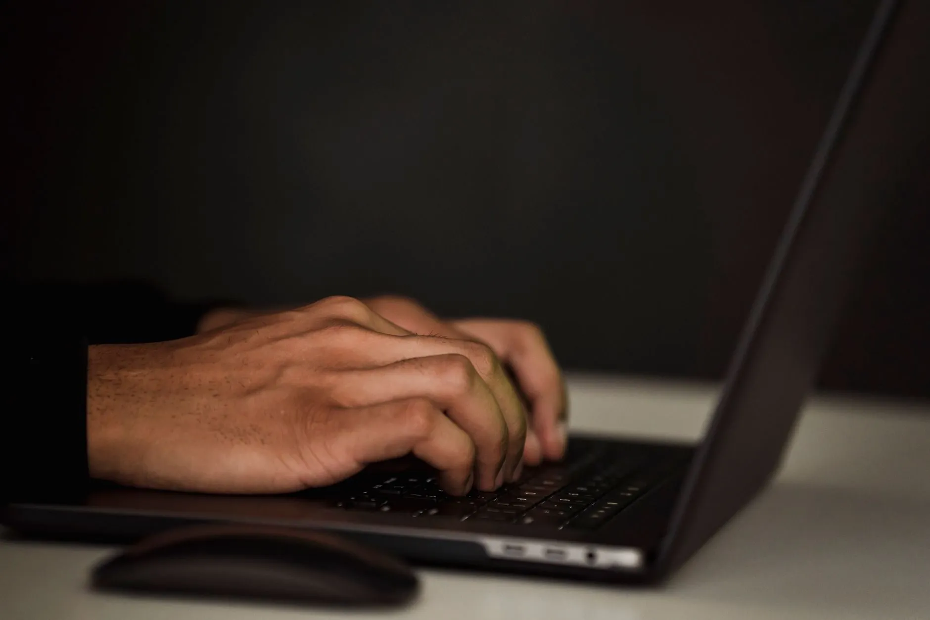 Hands typing on a dark laptop keyboard in a dim room