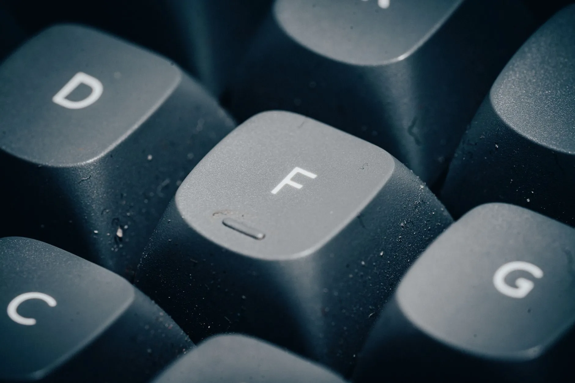 Close-up of dark keyboard keys D, F and G with dust on the caps
