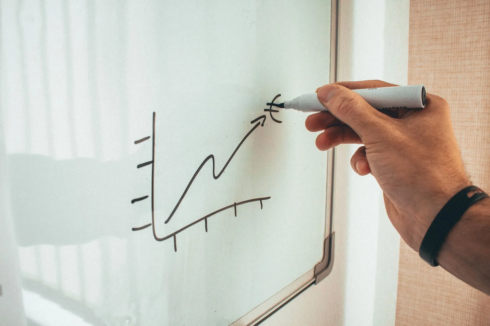 A hand drawing a rising line chart on a whiteboard with a marker