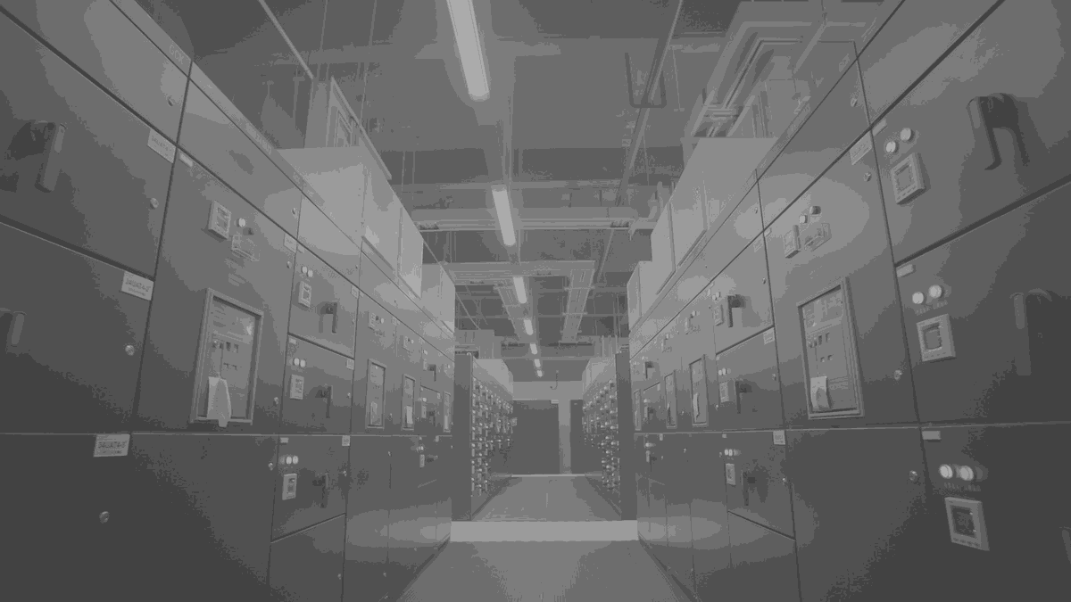 A switchgear aisle in a machine hall, cabinets running away to a lit end wall.